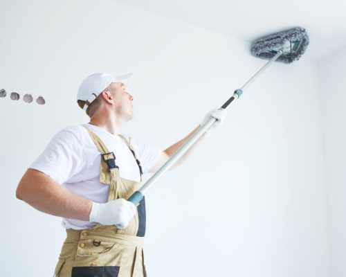 Gloved cleaner dusting the upper corner of a white room