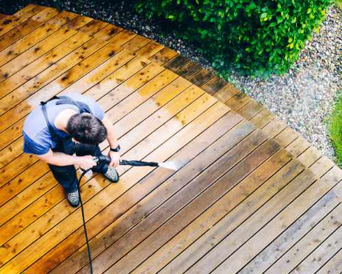 Man in overalls pressure washing wooden deck