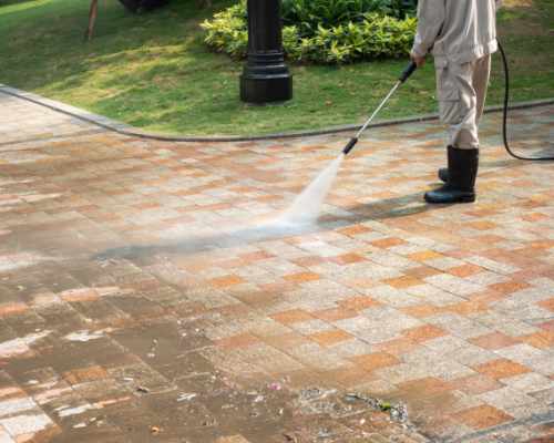 Pressure washer cleaning brick patio in black rubber boots