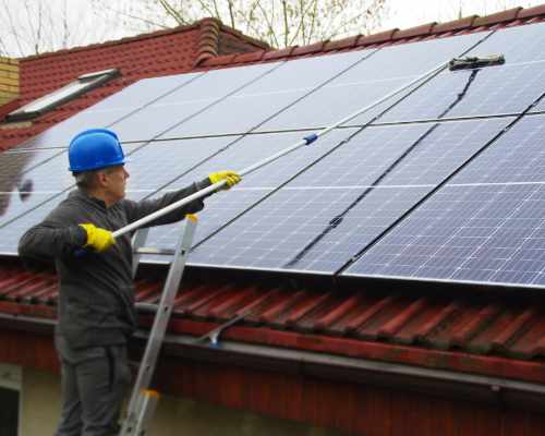 Man cleaning rooftop solar panels in blue hardhat